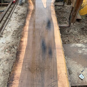 May include: A large slab of wood with a natural edge, showing the grain and color variations of the wood. The wood is wet and has a dark brown color with lighter brown streaks. The wood is marked with the text "5000" and "36".