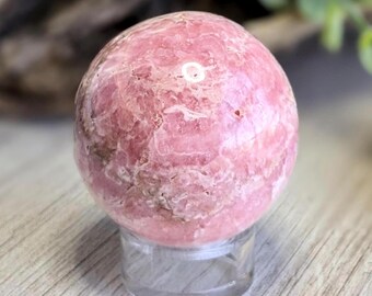 May include: A pink and white, polished, round,  rhodochrosite sphere on a clear stand.