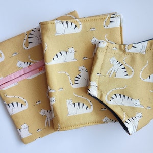A set of matching mask, mask pouch, and vaccine cardholder. The fabric on each item is yellow with white cats playing on it.