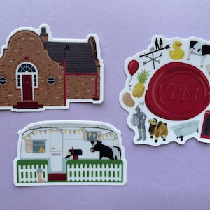 May include: Three die-cut stickers on a purple background. One depicts a brick building, another a white camper with a cow, and the third a red seal with various illustrations, including a duck, pineapple, and knight.
