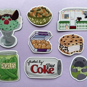 May include: A collection of colorful stickers featuring various food items and a camper. Includes an ice cream sundae, pasta, a box of nuggets, a cookie sandwich, pickles, a Diet Coke can, and a manatee.