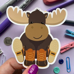 May include: A brown moose wearing brown boots with orange laces. The moose has large antlers and a friendly smile.