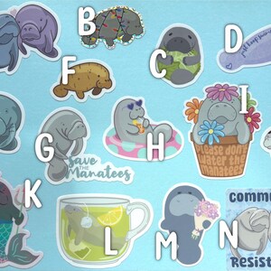 May include: A collection of fourteen manatee-themed stickers labeled A through N. Designs include manatees with flowers, in a teacup, as a mermaid, wearing sunglasses in a floatie, and with text like "save the manatees," "just keep swimming," and "community is resistance."