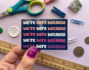 May include: A sticker with the phrase "we're here because" repeated five times in a rainbow of colors on a dark blue background.