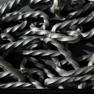 May include: A close-up of a twisted metal chain, with a dark, metallic finish. The chain is intertwined and overlapping, creating a textured and intricate pattern. The image is in black and white, highlighting the details of the chain.