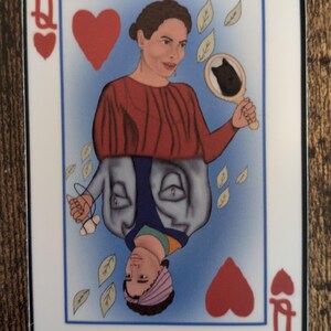 May include: A Queen of Hearts playing card with a woman's face on it. The woman is wearing a red shirt and a blue jacket. She is holding a mirror with a black cat in it. There are leaves falling around her.