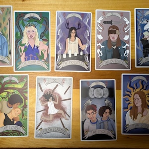 Puede incluir: Un conjunto de cartas del tarot con ilustraciones. Las cartas están tituladas con títulos como "El Superviviente", "La Herborista" y "La Sacerdotisa". Cada carta tiene un diseño único con figuras y símbolos.