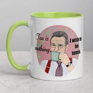 May include: White ceramic mug with a green rim. The mug features a cartoon illustration of a man drinking tea with the text "Tea is soothing. I wish to be tense."