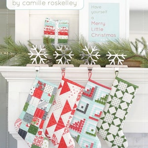 May include: A digital download pattern for making quilted Christmas stockings. The pattern is called "Merry Stockings 2" and is described as "super simple quilted stockings". The image shows three stockings hanging on a white fireplace mantel. The stockings are made with colorful patchwork fabric in red, green, blue, and white.