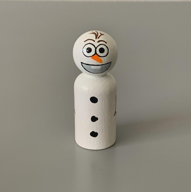 May include: A handcrafted wooden snowman figurine. The snowman has a white body with three black dots and painted arms. The head features a smiling face with black eyes, a carrot nose, and brown hair. A whimsical winter decoration.