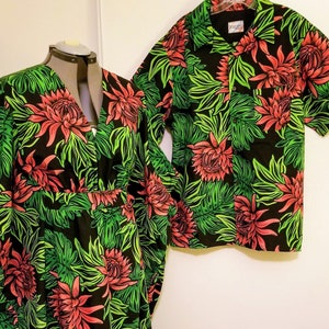 Op de afbeelding: Een bijpassende set zwarte en groene kleding met een bloemenprint met rode bloemen en groene bladeren. De set bevat een lange jurk en een shirt met korte mouwen. De tekst "VOLCANO DESIGNS SAN DIEGO" is zichtbaar in de rechterbenedenhoek van de afbeelding.
