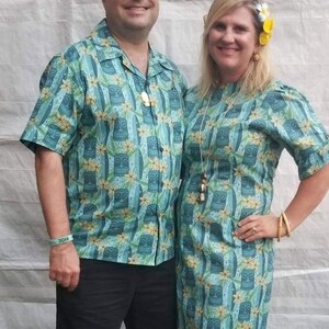 May include: A couple wearing matching blue and green shirts with a tiki design. The man is wearing a white sailor hat. The woman is wearing a flower in her hair.