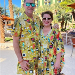 May include: A couple wearing matching yellow, green and red patterned shirts with geometric designs. The man is wearing a short-sleeved shirt and the woman is wearing a long-sleeved dress. They are both wearing sunglasses.