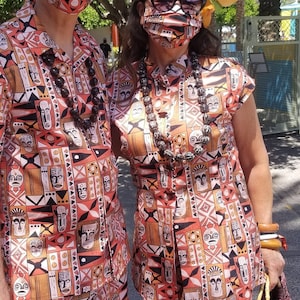 May include: A couple wearing matching orange, black, and white patterned shirts with a Polynesian design. The shirts feature a repeating pattern of stylized faces and geometric shapes. Both people are wearing face masks.