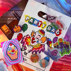 May include: A white party bag with the words "PARTY BAG" and a clown illustration. The image includes various stickers and pins with Halloween and cartoon themes, along with wrapped candies.