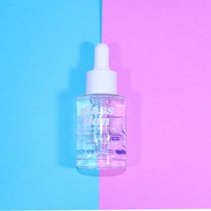 Puede incluir: Una botella de vidrio transparente con un gotero blanco y una etiqueta que dice "glass skin" suero hidratante para la piel con 2% de &aacute;cido hialur&oacute;nico. La botella est&aacute; sobre un fondo azul y rosa.