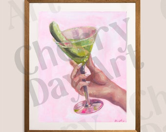 May include: A framed art print featuring a green cocktail in a martini glass with a pickle garnish. The painting has a pink background and a hand holding the glass. The frame is brown.