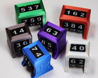 May include: A collection of six mechanical life counters in green, red, purple, blue, white, and grey. Each rectangular plastic frame houses rotating black number wheels with white digits, displaying various values like 537, 162, 14, 63, 74, and 40.