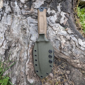 Könnte beinhalten: Ein grünes Messerfutteral mit schwarzen Druckknöpfen und einem braunen, strukturierten Griff. Das Futteral ist aus strapazierfähigem Material gefertigt und hat einen sicheren Verschluss.