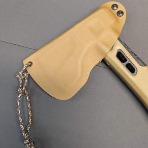 May include: A tan leather sheath with a green and brown rope attached. The sheath has two black snaps and is designed to hold a small axe.