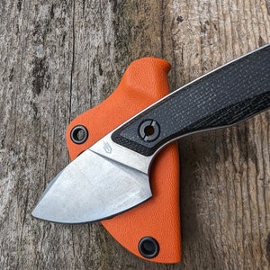 May include: A small, black and silver pocket knife with an orange sheath. The knife has a black, textured handle and a silver blade.