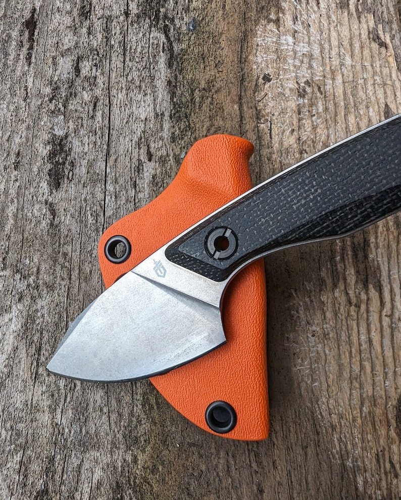 May include: A small, black and silver pocket knife with an orange sheath. The knife has a black, textured handle and a silver blade.