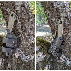 May include: A black leather knife sheath with a brown leather strap and a tan leather handle. The sheath is attached to a tree trunk with a green and brown camouflage paracord.