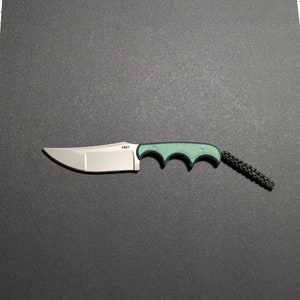 Puede incluir: Un cuchillo plegable con mango verde, hoja plateada y un cord&oacute;n de seguridad negro. El cuchillo tiene la palabra "CRKT" impresa en la hoja.