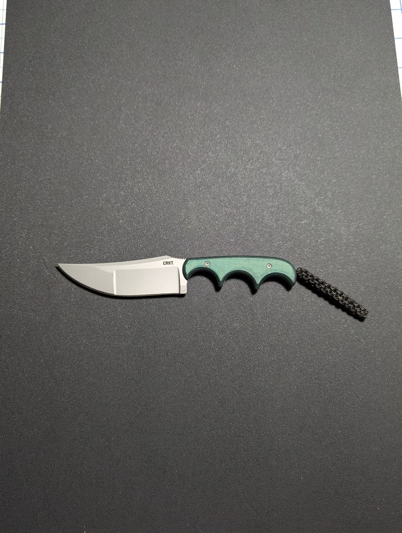 Puede incluir: Un cuchillo plegable con mango verde, hoja plateada y un cord&oacute;n de seguridad negro. El cuchillo tiene la palabra "CRKT" impresa en la hoja.