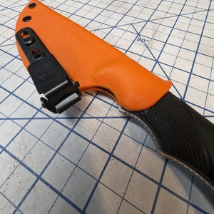 May include: An orange knife sheath with a black clip and a black knife handle with a textured pattern.