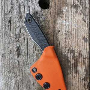 May include: A black and gray pocket knife with a carbon fiber handle and an orange leather sheath. The sheath has three black snaps.