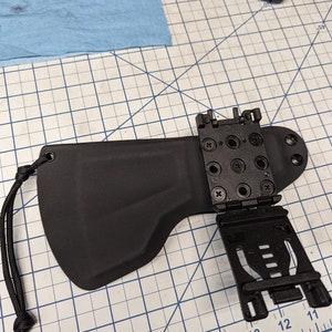 Puede incluir: Una funda de cuero negra con un accesorio de clip de plástico negro. La funda tiene un lazo para un cinturón y una correa para una pierna. El accesorio de clip tiene una serie de agujeros para ajustar la altura de la funda.