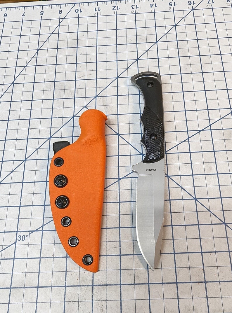 May include: A black handled knife with a silver blade and a black and orange sheath. The knife has a 4600723A serial number.