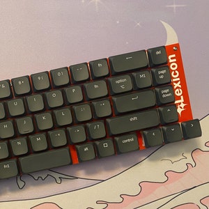 Könnte beinhalten: Eine schwarze mechanische Tastatur mit roten Akzenten und einem Lexicon-Logo. Die Tastatur hat ein Standardlayout mit Funktionstasten, Pfeiltasten und einem Nummernblock.