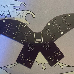May include: A black circuit board with a butterfly design and the text "36141218-7158-248418" printed on it.