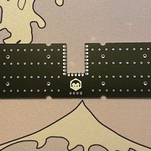 May include: A black circuit board with a U-shaped cutout in the center. The board has a hexagonal logo with the text "+++**" inside. The board has many small holes for soldering components.