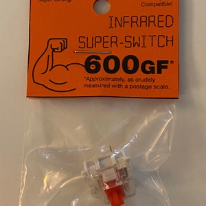 May include: A white and orange mechanical keyboard switch labeled "INFRARED SUPER-SWITCH 600GF*" with the text "Cherry MX Compatible!" and "Super-Strong!" on the packaging.