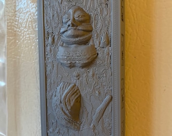 May include: A 3D printed wall decor featuring a gray Jabba the Hutt from Star Wars. The decor is framed in a gray frame.