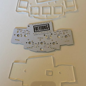 Peut inclure: Une carte de circuit imprimé blanche avec le texte "REVINGS rev1.0 Designed by glips 2021" et les mots "TH", "SHD" et "RESET".