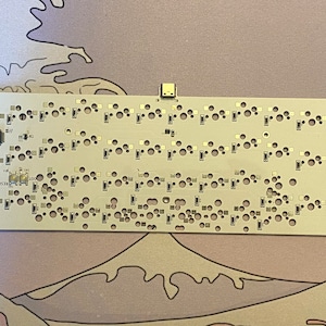 以下が含まれることがあります： USBコネクタと小さな穴がいくつかある白い回路基板。基板には小さな黒いチップと「RESET」という文字が印刷されています。