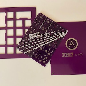 Könnte beinhalten: Drei violette Acrylplatten für einen benutzerdefinierten Tastaturaufbau. Die Platten sind mit "SOYUZ Numpad Kit" und "SOYUZ by ai03" beschriftet.