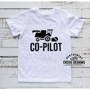 May include: White t-shirt with a black graphic of a combine harvester and the text "CO-PILOT". The shirt also features the "Montgomery Creek Designs" logo. A casual, everyday wear tee.