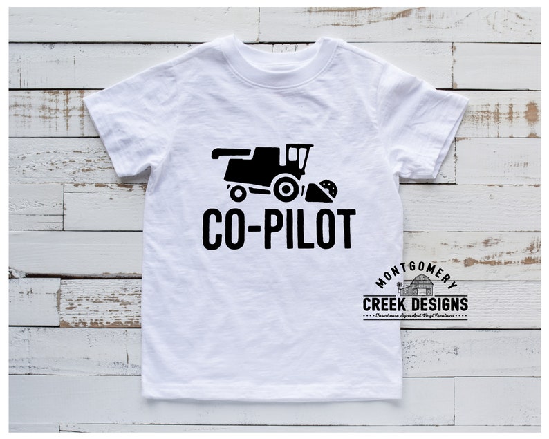 May include: White t-shirt with a black graphic of a combine harvester and the text "CO-PILOT". The shirt also features the "Montgomery Creek Designs" logo. A casual, everyday wear tee.