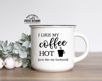 May include: White ceramic mug with a black rim and handle. The mug has a black graphic that says "I like my coffee HOT (just like my husband)".