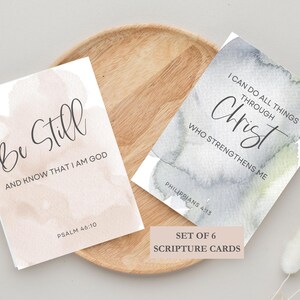 May include: Set of six watercolor scripture cards with inspirational quotes. The cards feature a light pink and gray watercolor background with black calligraphy. The quotes are "Be Still and Know That I Am God" (Psalm 46:10) and "I Can Do All Things Through Christ Who Strengthens Me" (Philippians 4:13).