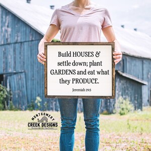 May include: A wooden sign with a white background and black text that reads "Build HOUSES & settle down; plant GARDENS and eat what they PRODUCE. Jeremiah 29:5".
