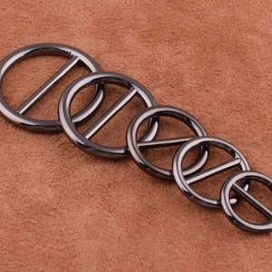 May include: Five black metal rings with a center bar, arranged in descending size order. The rings are smooth and have a polished finish.
