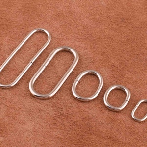 May include: Five silver metal oval rings of different sizes. The rings are arranged in a row from largest to smallest.