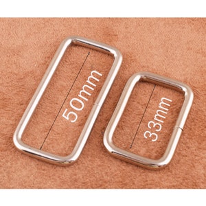 May include: Two silver metal rectangular rings, one measuring 50mm and the other 33mm. The rings are on a brown surface.