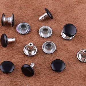 Puede incluir: Surtido de remaches de metal negro y plateado. Los remaches tienen una cabeza redonda y un poste que se puede martillar en su lugar. Los remaches se utilizan comúnmente para unir cuero, tela u otros materiales.